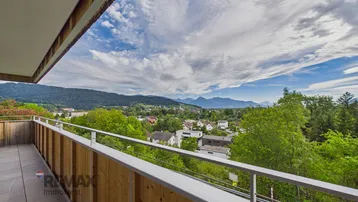 Geräumiger Balkon mit Holzelementen und weitem Blick über das Tal und die umliegenden Berge.