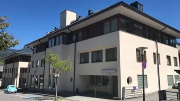 Modernes Mehrfamilienhaus mit heller Putzfassade, großen Fenstern und Blick auf die umliegende Berglandschaft.