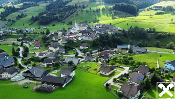 Luftaufnahme eines malerischen Dorfes in einer grünen Hügellandschaft mit vielen Häusern und einer Kirche.