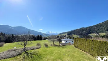 Weitläufiger Blick über grüne Wiesen und Berge unter strahlend blauem Himmel.