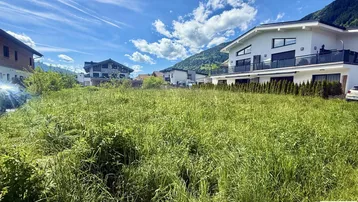 Großes unbebautes Grundstück mit Blick auf moderne Häuser und die umliegende Berglandschaft.