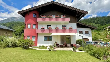 Charmantes Haus mit roter Fassade, Balkonen und gepflegtem Gartenbereich unter blauem Himmel.