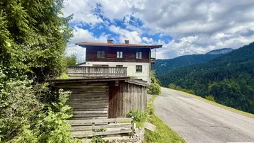 Haus in den Bergen mit Holzanbau und weitem Blick auf die bewaldete Landschaft.
