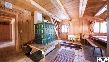 Gemütlicher alpiner Wohnbereich mit traditionellem Kachelofen, Holzbalken und viel natürlichem Licht.