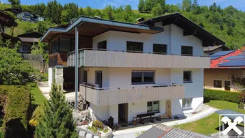 Modernes Wohnhaus mit mehreren Balkonen und Holzverkleidung in alpiner Umgebung.