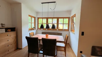 Heller Essbereich mit Holztisch, bequemer Sitzbank und Blick ins Grüne durch mehrere Fenster.