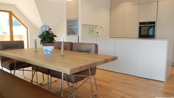 Heller offener Wohn- und Essbereich mit Holztisch, Lederbänken und integrierter moderner Küche.