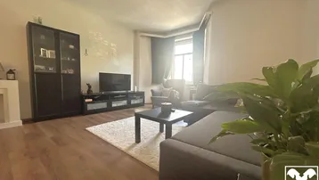 Helles Wohnzimmer mit Holzboden, gemütlichem Sofa und Fernseher, ideal für entspannte Abende.