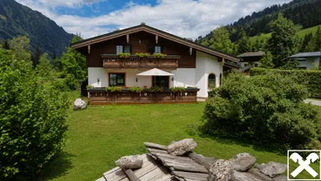 Traditionelles Alpenhaus mit Holzbalkonen, Blumenkästen und gepflegtem Vorgarten in bergiger Umgebung.