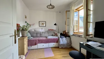 Helles Kinder- oder Gästezimmer mit Holzboden, Tagesbett und Blick ins Grüne.