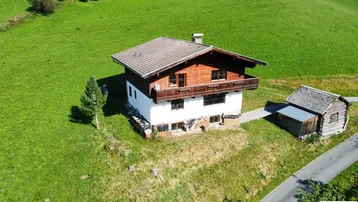 Traditionelles Haus im Chalet-Stil mit Satteldach und Holzbalkonen, umgeben von grünen Wiesen.