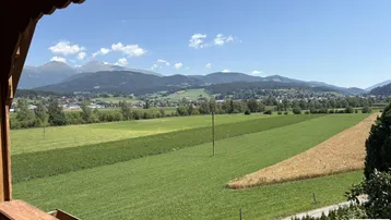 Panoramablick vom Balkon über weite grüne Felder und die umliegende Berglandschaft unter blauem Himmel.
