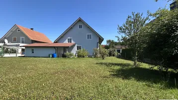 Großer Gartenbereich mit Rasenfläche und Blick auf das Einfamilienhaus unter blauem Himmel.