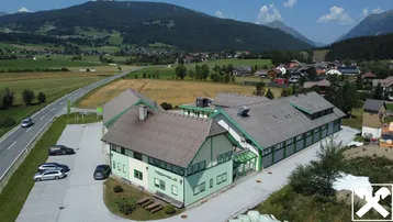 Luftaufnahme eines modernen Gebäudekomplexes in ländlicher Umgebung mit Bergen im Hintergrund und viel Grün.