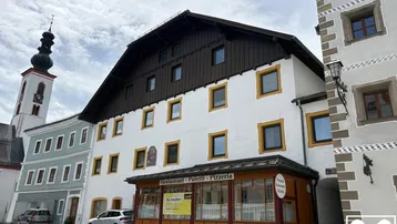 Fassade eines traditionellen Gebäudes mit Restaurant im Erdgeschoss und Kirchturm im Hintergrund.