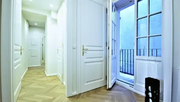 Heller Flur mit Fischgrätparkett und Zugang zu einem französischen Balkon durch eine offene Tür.