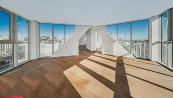 Helles, leeres Zimmer mit Holzboden und großen Fenstern, die viel Tageslicht hereinlassen.