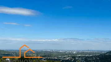 Panoramablick über eine weite Stadtlandschaft mit grünen Hügeln unter blauem Himmel.