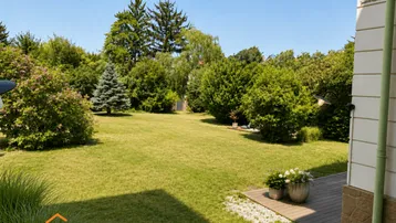 Großer, gepflegter Garten mit weitläufiger Rasenfläche und altem Baumbestand an einem sonnigen Tag.