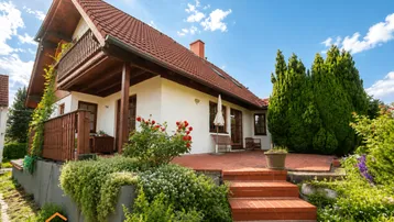 Charmantes Einfamilienhaus mit großer Terrasse, Garten und Balkon unter strahlend blauem Himmel.