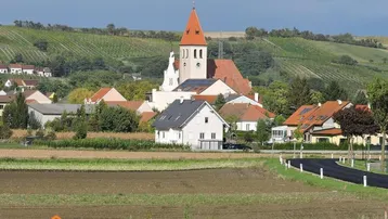 Panoramablick auf ein malerisches Dorf mit Kirche, umgeben von Feldern und Weinbergen.