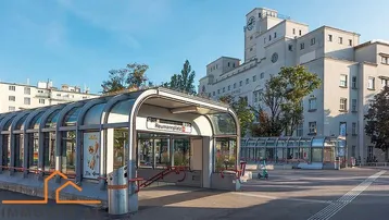 U-Bahn-Station Reumannplatz mit einem großen, hellen Gebäude und Uhrturm im Hintergrund in einem städtischen Gebiet.
