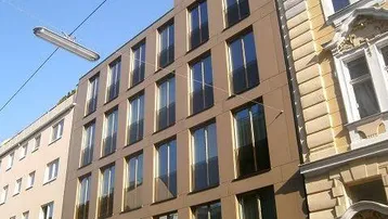 Moderne Fassade eines Neubaus mit vielen Fenstern, umgeben von traditionellen Gebäuden.