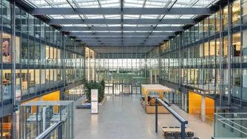 Großzügiges, modernes Atrium mit Glasdach, vielen Büroetagen und hellem Empfangsbereich.