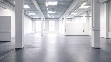 Geräumige, leere Industriehalle mit hohen Decken, Betonboden und Oberlichtern, ideal für gewerbliche Nutzung.