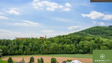 Weitläufiger Blick über grüne Hügel, Felder und eine historische Klosteranlage unter blauem Himmel.