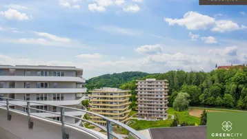 Weitläufiger Blick vom Balkon auf grüne Hügel, weitere Gebäude und die umliegende Landschaft.