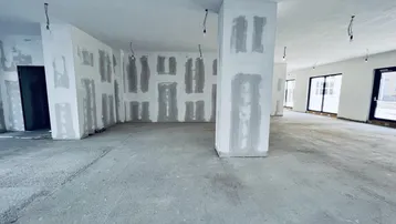 Großer, offener Gewerberaum im Rohbau mit Betonboden und großen Fenstern, bereit für den Ausbau.