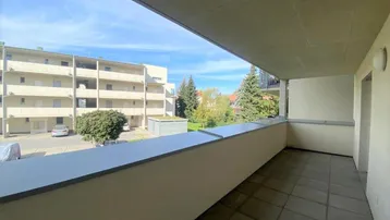 Geräumiger Balkon mit Fliesenboden und Blick auf die umliegenden Gebäude und Bäume.