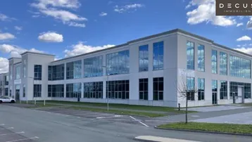Modernes Bürogebäude mit großer Glasfassade und weitläufigen Parkplätzen unter blauem Himmel.
