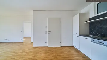 Heller offener Wohnbereich mit integrierter Küche, Parkettboden und weißen Schränken.