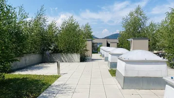Gepflasterte Dachterrasse mit Grünflächen und Blick auf die Umgebung unter blauem Himmel.