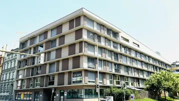 Modernes Eckgebäude mit mehreren Etagen und großen Fenstern in städtischer Umgebung.