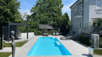 Großer Außenbereich mit modernem Pool, gefliester Terrasse und üppigem Grün, ideal für Entspannung im Freien.