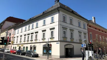 Historisches Eckgebäude an einer belebten Straße mit traditioneller Architektur und vielen Fenstern.