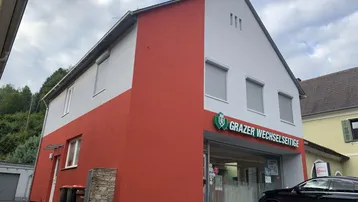 Gebäudeansicht mit rot-grauer Fassade und Geschäftsfläche im Erdgeschoss.
