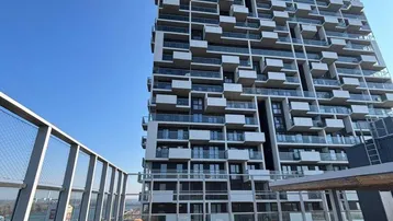 Moderne Hochhausfassade mit zahlreichen Balkonen und einer Dachterrasse mit Panoramablick.