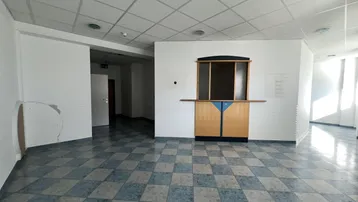 Geräumiger Empfangsbereich mit einem hölzernen Tresen und einem blau-grau gefliesten Boden.