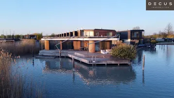 Moderne schwimmende Häuser mit Holzfassaden und großzügigen Terrassen am Wasser.