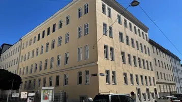 Mehrstöckiges Gebäude mit heller Fassade und vielen Fenstern an einer städtischen Straße.