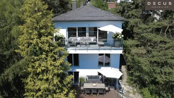 Modernes Wohnhaus mit mehreren Balkonen und Terrassen, umgeben von üppigem Grün und hohen Bäumen.