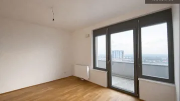 Helles Zimmer mit Parkettboden, großen Fenstern und Zugang zu einem kleinen Balkon mit Stadtblick.
