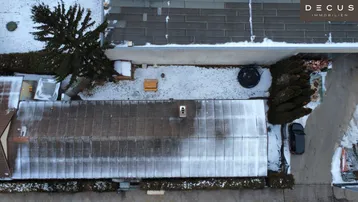 Luftaufnahme von oben zeigt Dächer von Gebäuden und einen verschneiten Hofbereich mit einem Auto.