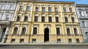 Historisches Mehrfamilienhaus mit gelber Fassade und vielen Fenstern an einer Stadtstraße.