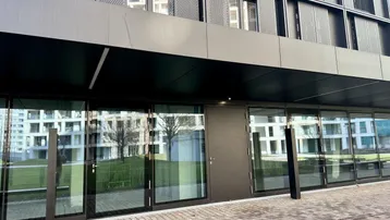 Moderne Geschäftsfassade mit großen Glasfronten und dunklen Metallverkleidungen, die eine einladende Eingangszone bilden.