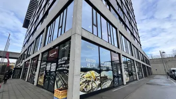 Modernes Gebäude mit großen Glasfenstern und Werbeplakaten für ein Restaurant im Erdgeschoss.
